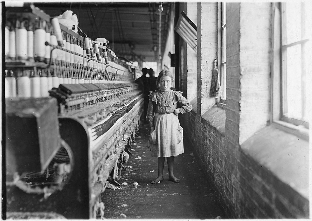 Barefoot girl next to a long row of machinery